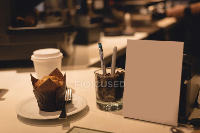Muffin y granos de café en el mostrador en la cafetería - foto de stock