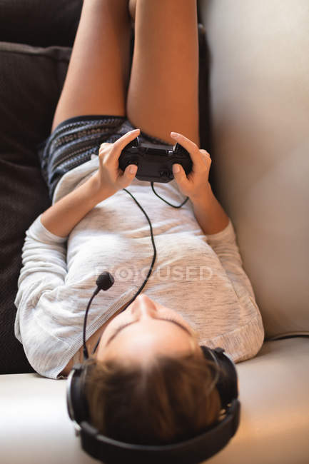 Mujer jugando videojuego con auriculares en la sala de estar en casa - foto de stock