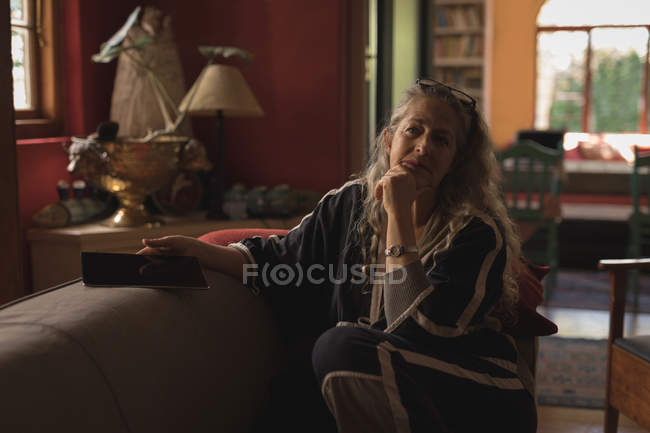 Портрет зрелой женщины, сидящей с цифровой табличкой на диване — стоковое фото