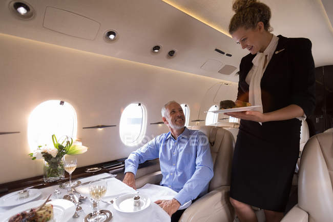 Бортпроводник, подающий еду бизнесмену на частном самолете — стоковое фото