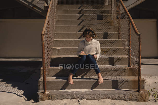 Adolescente chica leyendo libro en la escalera en la playa - foto de stock