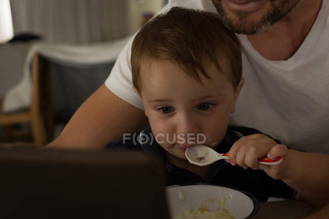 Отец и сын завтракают, используя цифровой планшет дома — стоковое фото