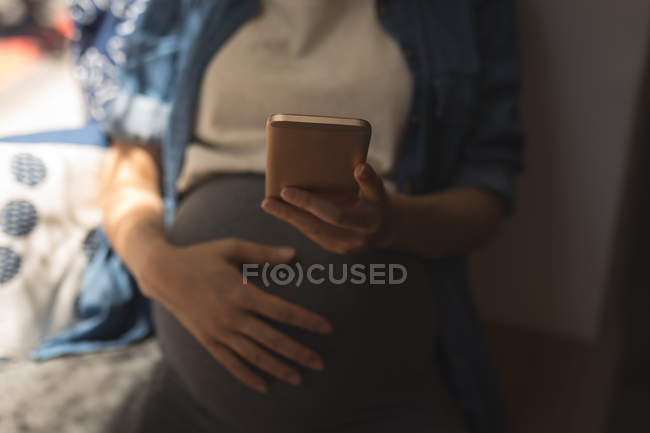 Sección media de la mujer embarazada usando el teléfono móvil en la cafetería - foto de stock