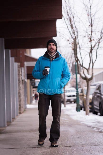 Чоловік ходить під час кави на тротуарі взимку . — стокове фото