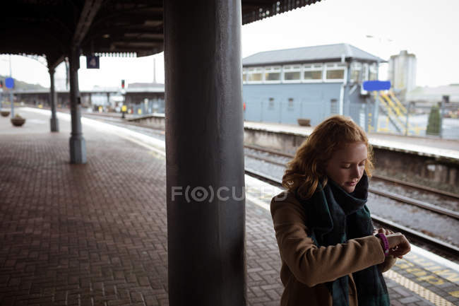 Joven mujer de pie en la plataforma ferroviaria comprobar el tiempo en su reloj inteligente - foto de stock