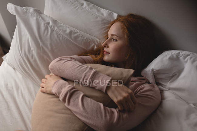 Thoughtful woman relaxing on bed in bedroom at home — Stock Photo