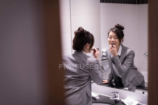 Businesswoman applying lipstick in front of mirror in bathroom — Stock Photo