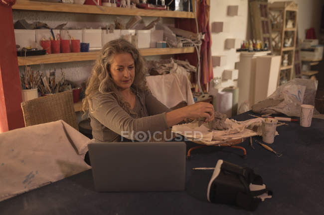 Töpferin schaut auf Laptop, während sie zu Hause Ton formt — Stockfoto