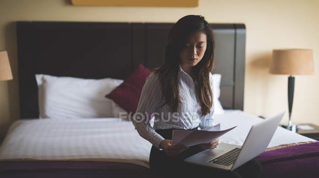 Бизнесмен читает документы во время работы на ноутбуке в гостиничном номере — стоковое фото