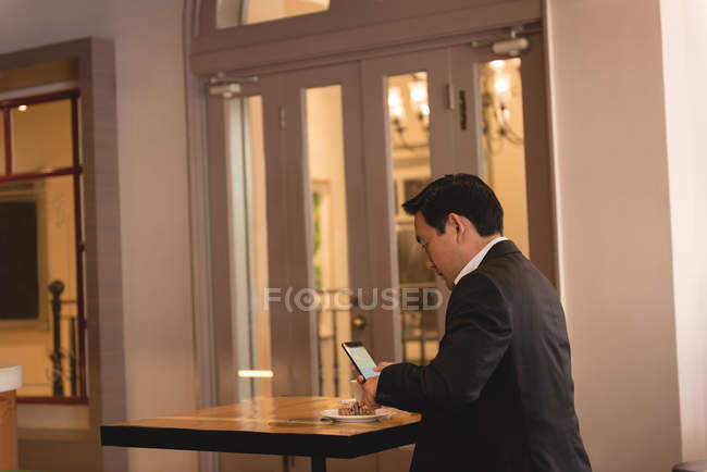 Uomo d'affari che utilizza il telefono cellulare mentre prende il caffè in caffetteria — Foto stock