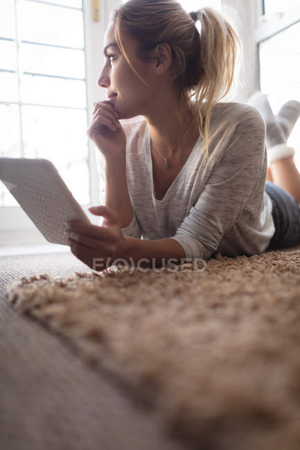 Женщина с помощью цифрового планшета, лежа на полу дома — стоковое фото
