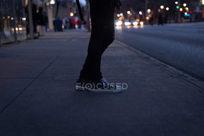 Baixa seção de mulher de pé na rua da cidade ao entardecer — Fotografia de Stock