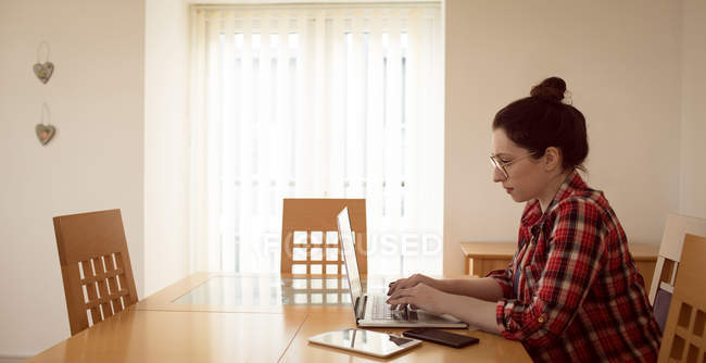 Belle femme dans les lunettes en utilisant un ordinateur portable à la maison . — Photo de stock