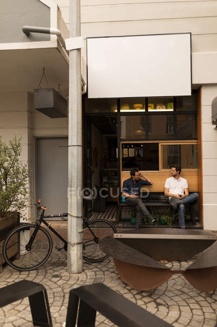 Uomini che interagiscono su panca in caffè marciapiede — Foto stock
