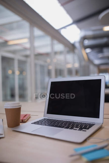Ноутбук и одноразовая чашка на столе в офисе — стоковое фото