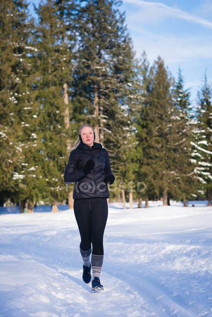 Mulher atlética correndo na paisagem nevada em um dia ensolarado — Fotografia de Stock
