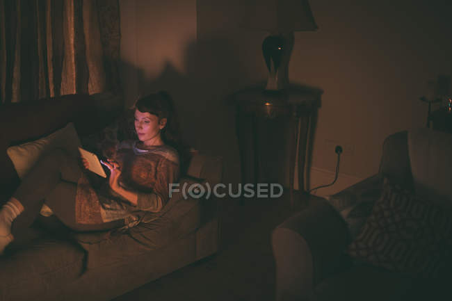 Donna che utilizza tablet digitale sul divano in soggiorno a casa — Foto stock