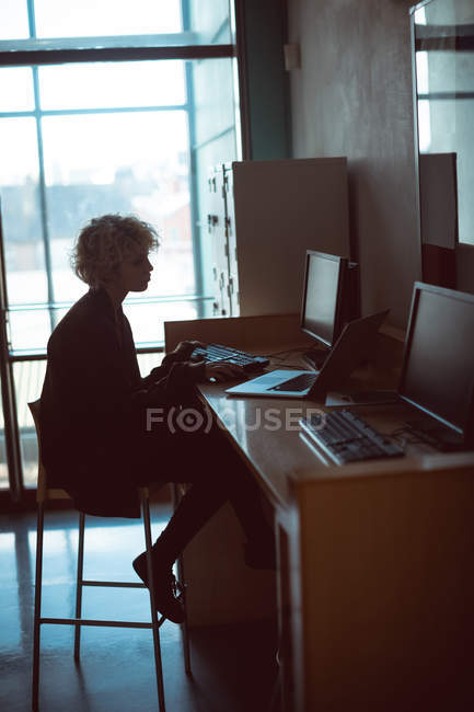 Жінка працює на комп'ютері за столом у бібліотеці — стокове фото