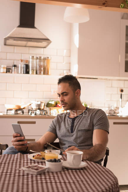 Чоловік використовує мобільний телефон під час сніданку на кухні вдома . — стокове фото