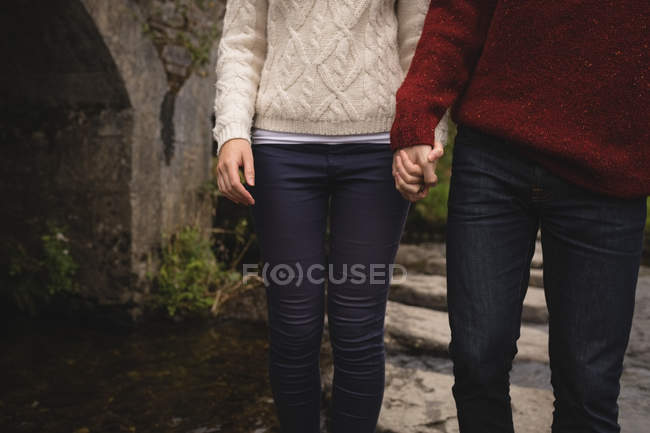 Sección media de la pareja cogida de la mano cerca de la orilla del río - foto de stock
