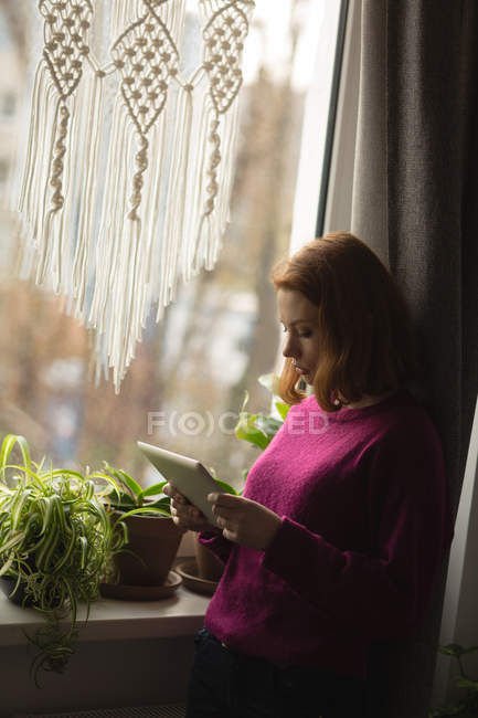 Frau nutzt digitales Tablet am Fenster zu Hause — Stockfoto