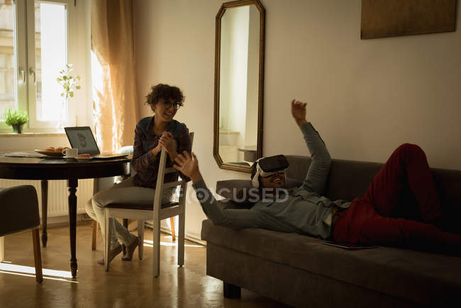 Жінка, дивлячись на людину при використанні віртуальної реальності гарнітуру у вітальні — стокове фото