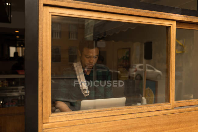 Male staff using laptop in cafe behind window glass — Stock Photo