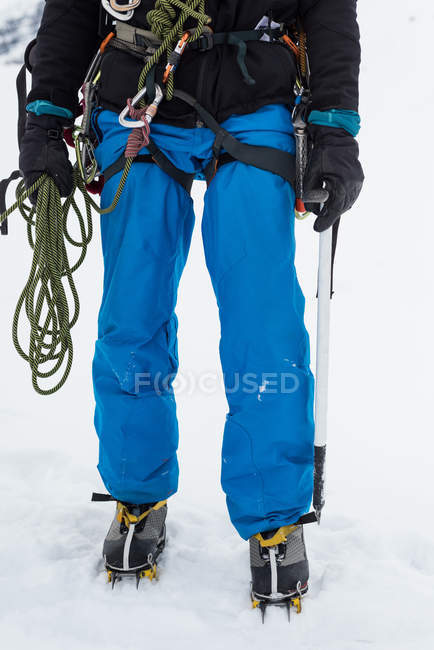 Чоловік альпініст стоїть з мотузкою і сокирою на засніженому регіоні взимку — стокове фото