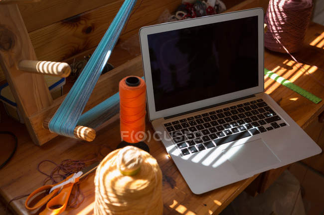 Close-up of laptop with weaving equipemts on desk — Stock Photo