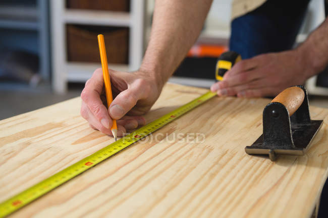 Sección media del carpintero macho que mide y marca la madera en taller - foto de stock