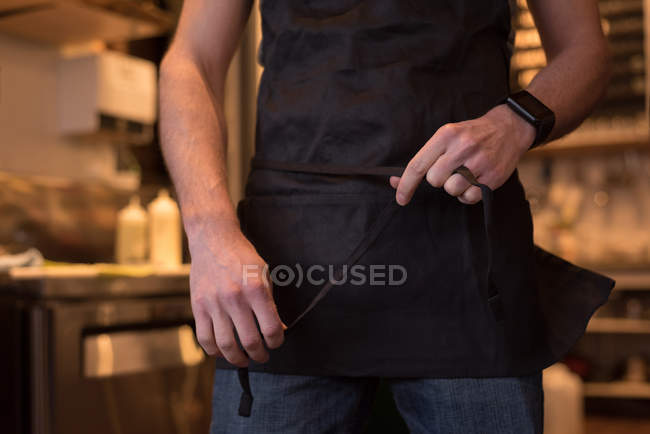Mittlerer Teil des männlichen Kellners trägt schwarze Schürze im Café. — Stockfoto