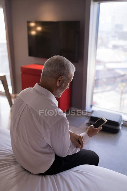 Homme d'affaires utilisant un téléphone intelligent sur le lit dans la chambre d'hôtel — Photo de stock