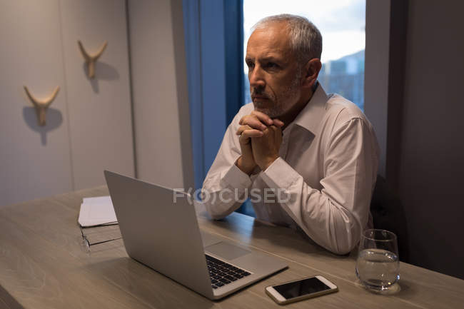 Geschäftsmann denkt tief nach, während er am Schreibtisch im Hotelzimmer sitzt — Stockfoto