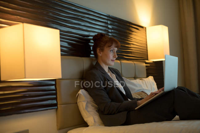Businesswoman using laptop on a bed in hotel room — Stock Photo