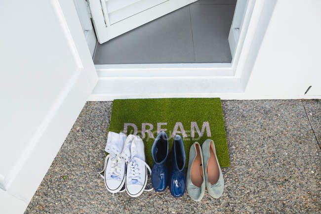 Varios zapatos guardados en una alfombra de la puerta delante de la puerta de la casa - foto de stock