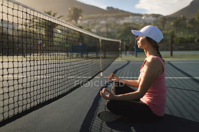 Jeune femme effectuant des exercices de yoga au court de tennis — Photo de stock