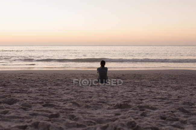 Vista trasera de la mujer sentada en la playa de arena al atardecer . - foto de stock