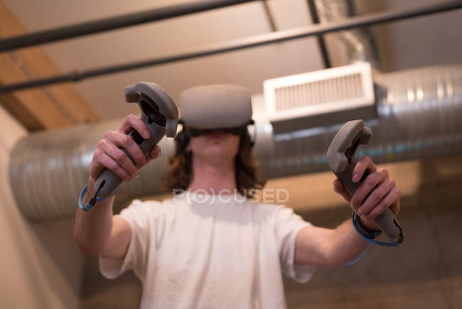 Vista de ángulo bajo del ejecutivo masculino usando auriculares de realidad virtual con controlador en la oficina . - foto de stock