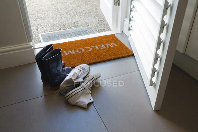 Différentes chaussures conservées sur un tapis de porte à la maison — Photo de stock