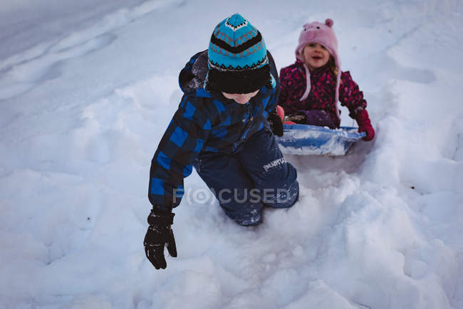 Мальчик тянет свою сестру в санях на блюдце зимой — стоковое фото