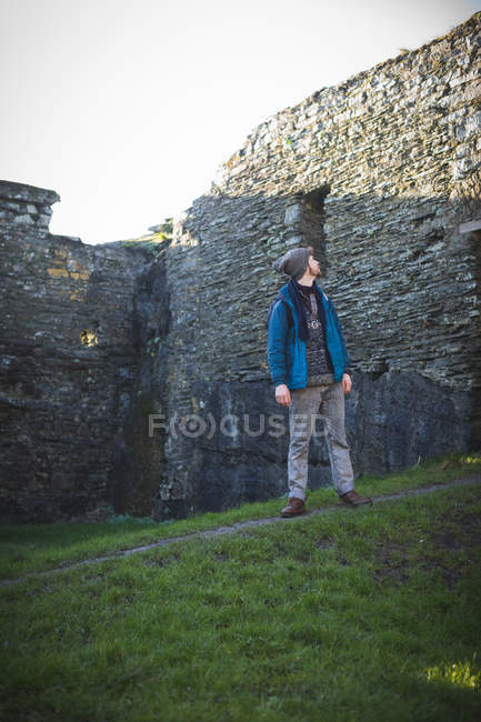 Jovem caminhante do sexo masculino em pé em ruínas antigas no campo — Fotografia de Stock