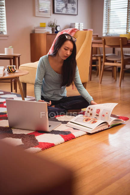 Donna che legge un libro di ricette in soggiorno a casa — Foto stock