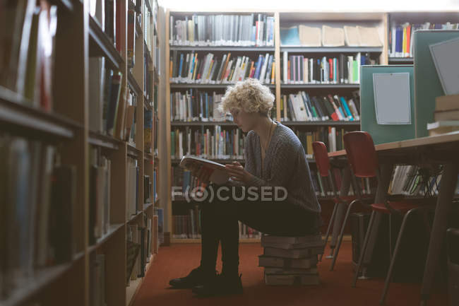 Mujer joven leyendo un libro en la biblioteca - foto de stock