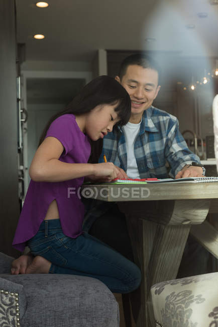 Padre ayudando a su hija a hacer los deberes en casa - foto de stock