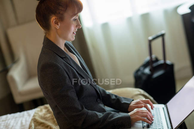 Femme d'affaires utilisant un ordinateur portable sur le lit dans la chambre d'hôtel — Photo de stock