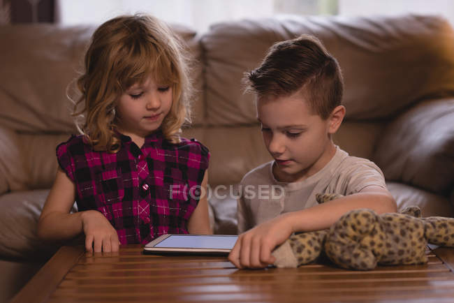 Niño y niña usando tableta digital en la sala de estar en casa - foto de stock