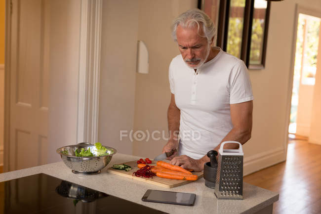 Homem sênior cortando vegetais na cozinha em casa — Fotografia de Stock