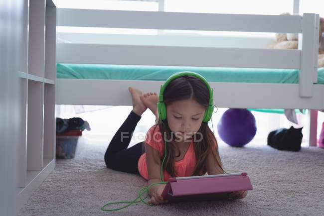 Menina idade elementar em fones de ouvido usando tablet digital no chão em casa — Fotografia de Stock