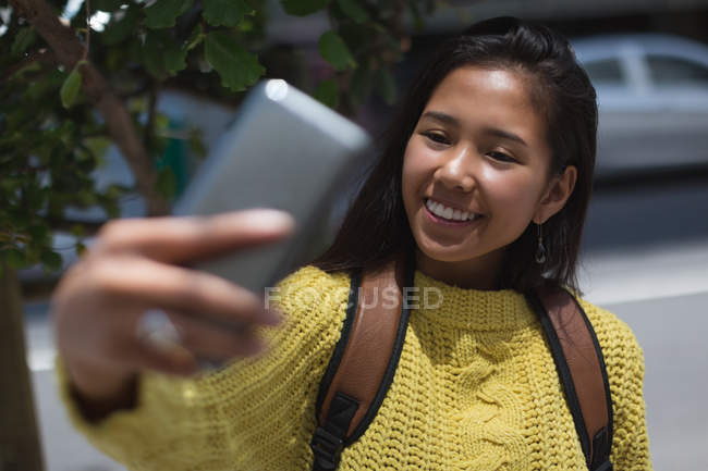 Teenage girl taking selfie with mobile phone in city — Stock Photo