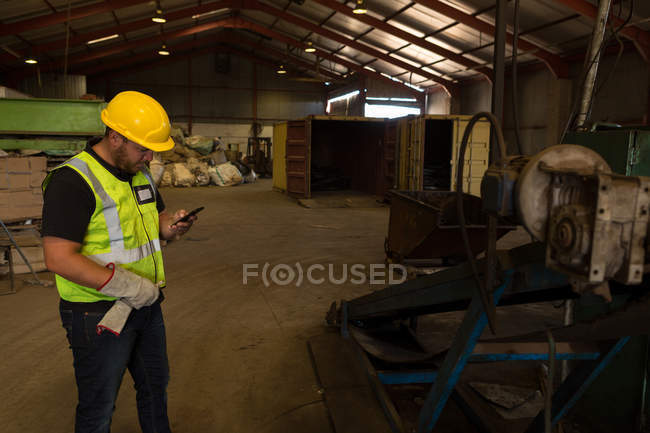Trabajador concentrado usando su teléfono móvil en el desguace - foto de stock